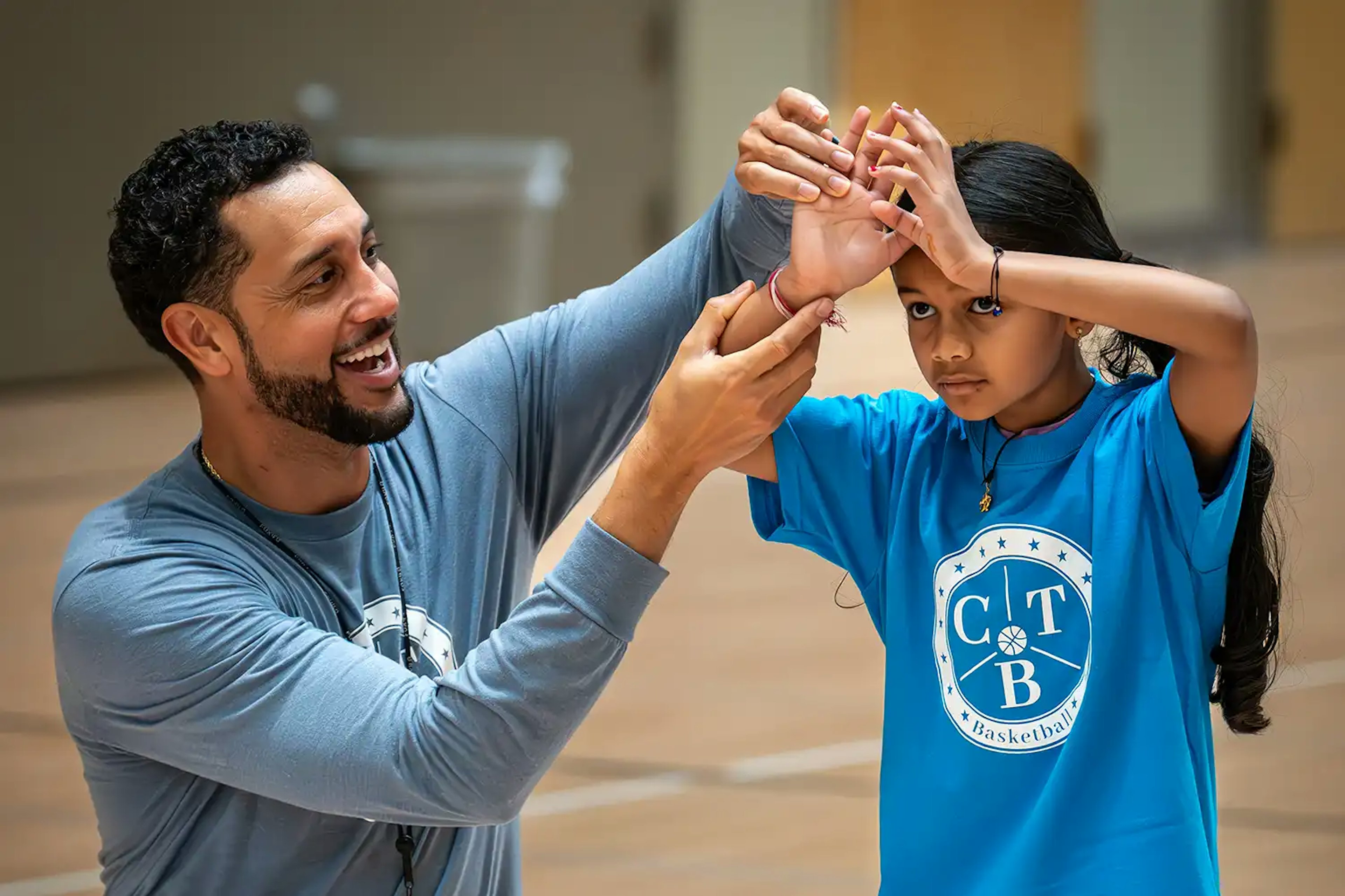 A picture of a coach teaching a young girl how to shoot a basketball